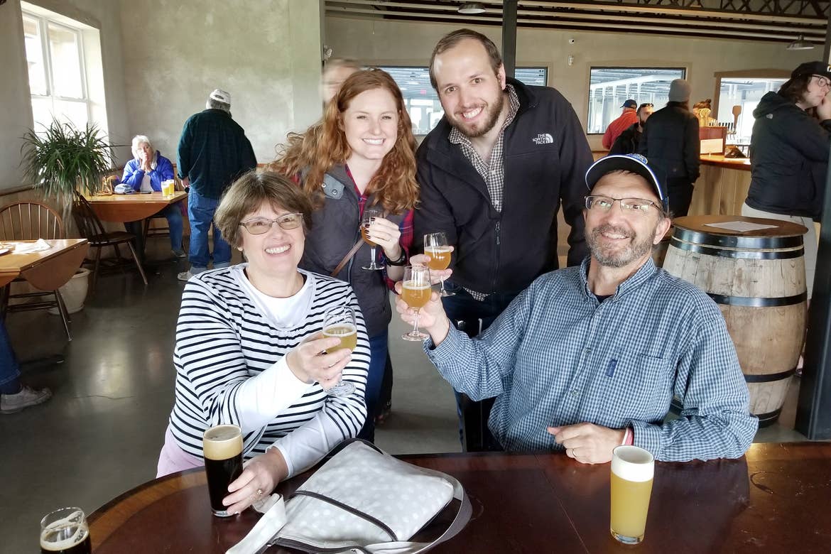 Two caucasian men (right) and two Caucasian women (left) hold up glasses of beer at Hill Farmstead Brewery in Vermont.