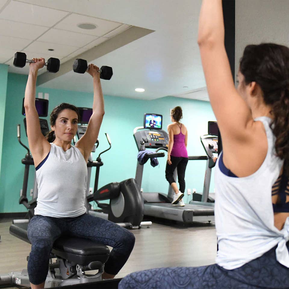 A woman lifting free weights at a fitness center in front of a mirror