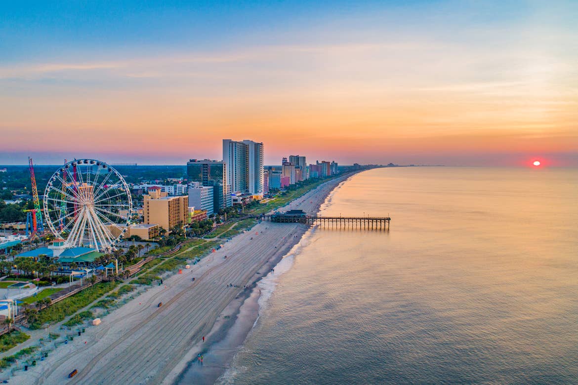 An aerial view of the boardwalk overlooking Myrtle Beach as the sun sets on the ocean.