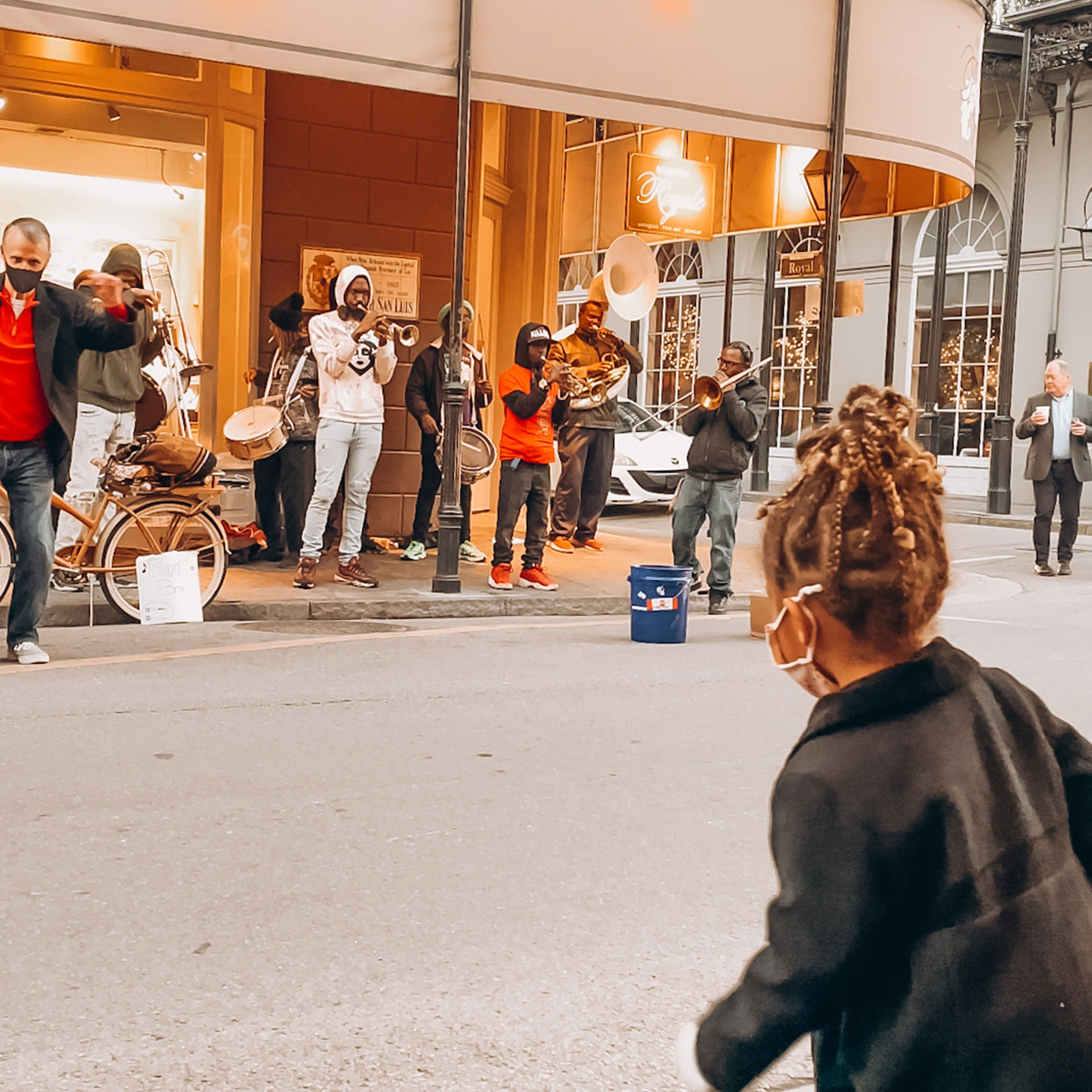 Featured Contributor, Sally Butan of @butanclan's daughter wears a mask and jacket while dancing to a live brass band on Bourbon St. in New Orleans, Louisiana.