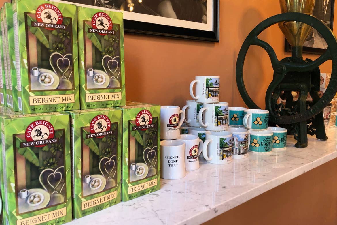 Multiple boxes of Cafe Beignet Mix on a countertop alongside branded mugs.