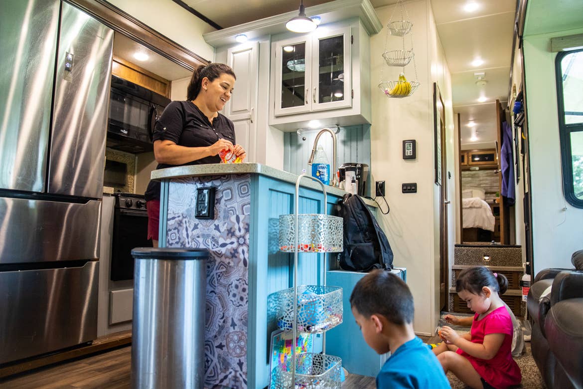 Angelica (left) preps in their RV kitchen while the children (bottom-right) play on the ground with their toys.