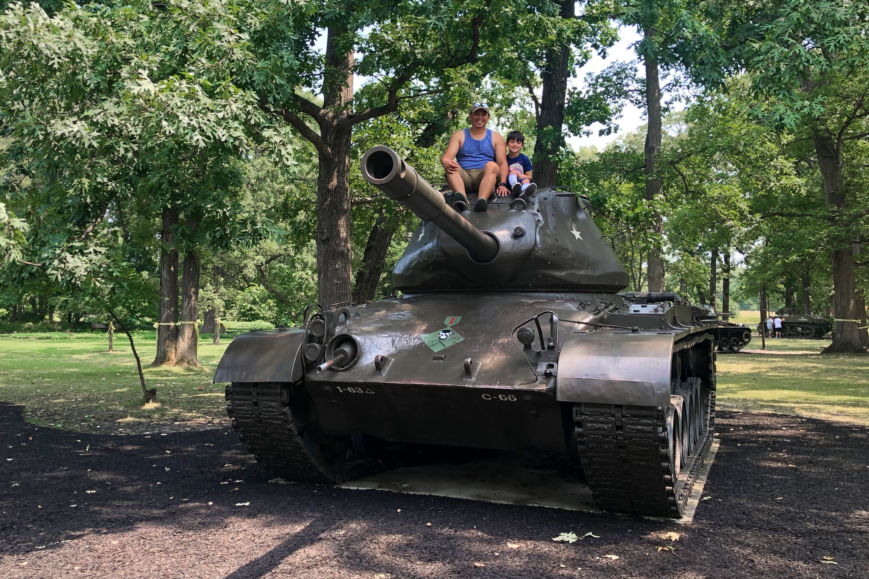 A man and child sit on the top of an old  US Army tank.