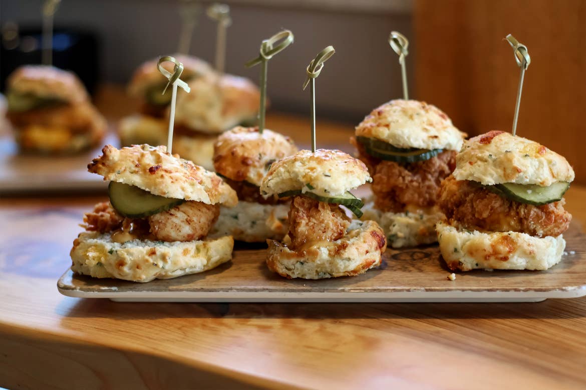 A woodgrain platter served with several mini-sliders with skewers.