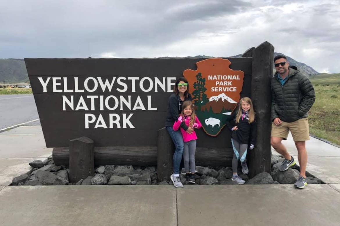 Chris (top-left) stands with Josh (top-right) and Kyndall (bottom-right) and Kylar (bottom-left) in front of Yellowstone National Park sign.