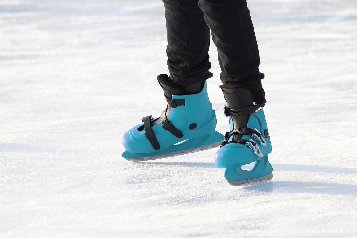 A child skates on ice wearing a black snow pants and a pair of blue ice skates.