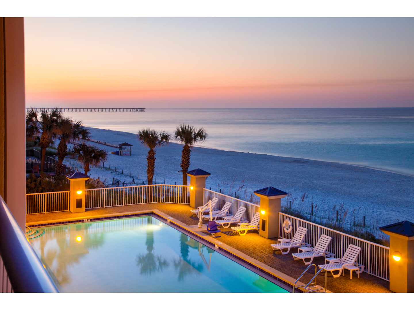 Sunsets over water behind a warmly lit pool deck.