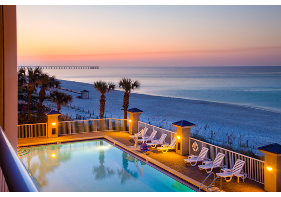 Sunsets over water behind a warmly lit pool deck.