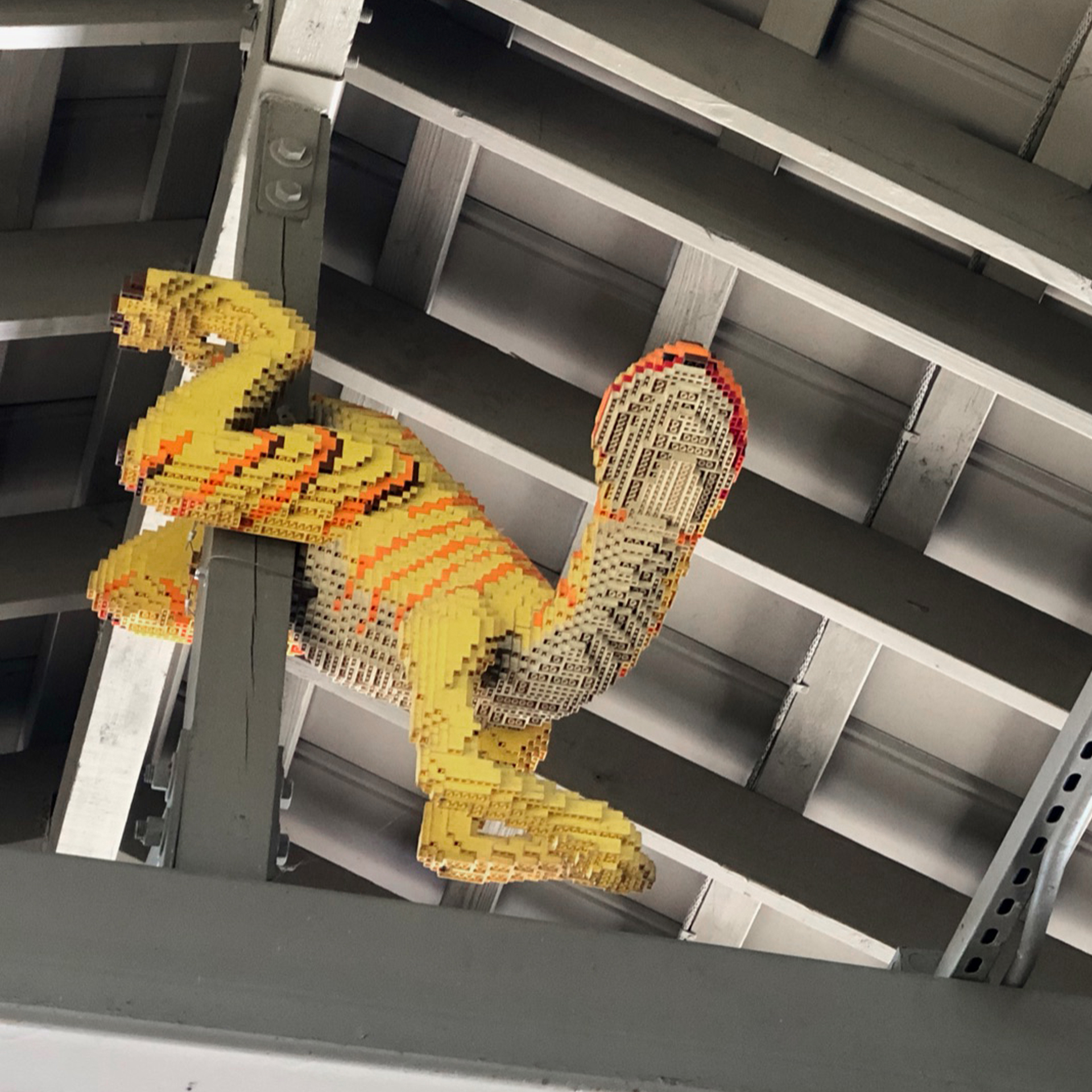 A dinosaur figurine made of LEGOS hangs on a structural beam.