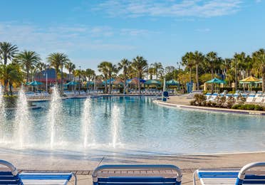 Pool with beach chairs and palm trees and Breezes Restaurant & Bar in West Village at Orange Lake Resort near Orlando, Florida.