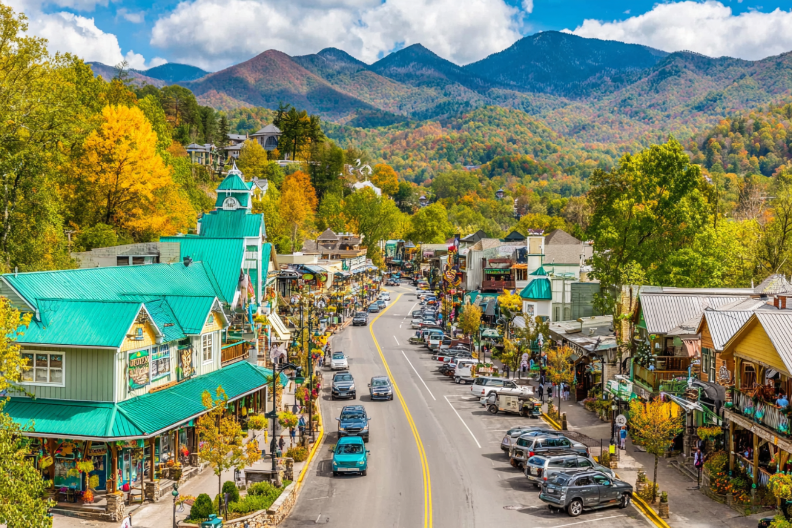 Colorful downtown Gatlinburg street with shops, cars, and Smoky Mountains backdrop.