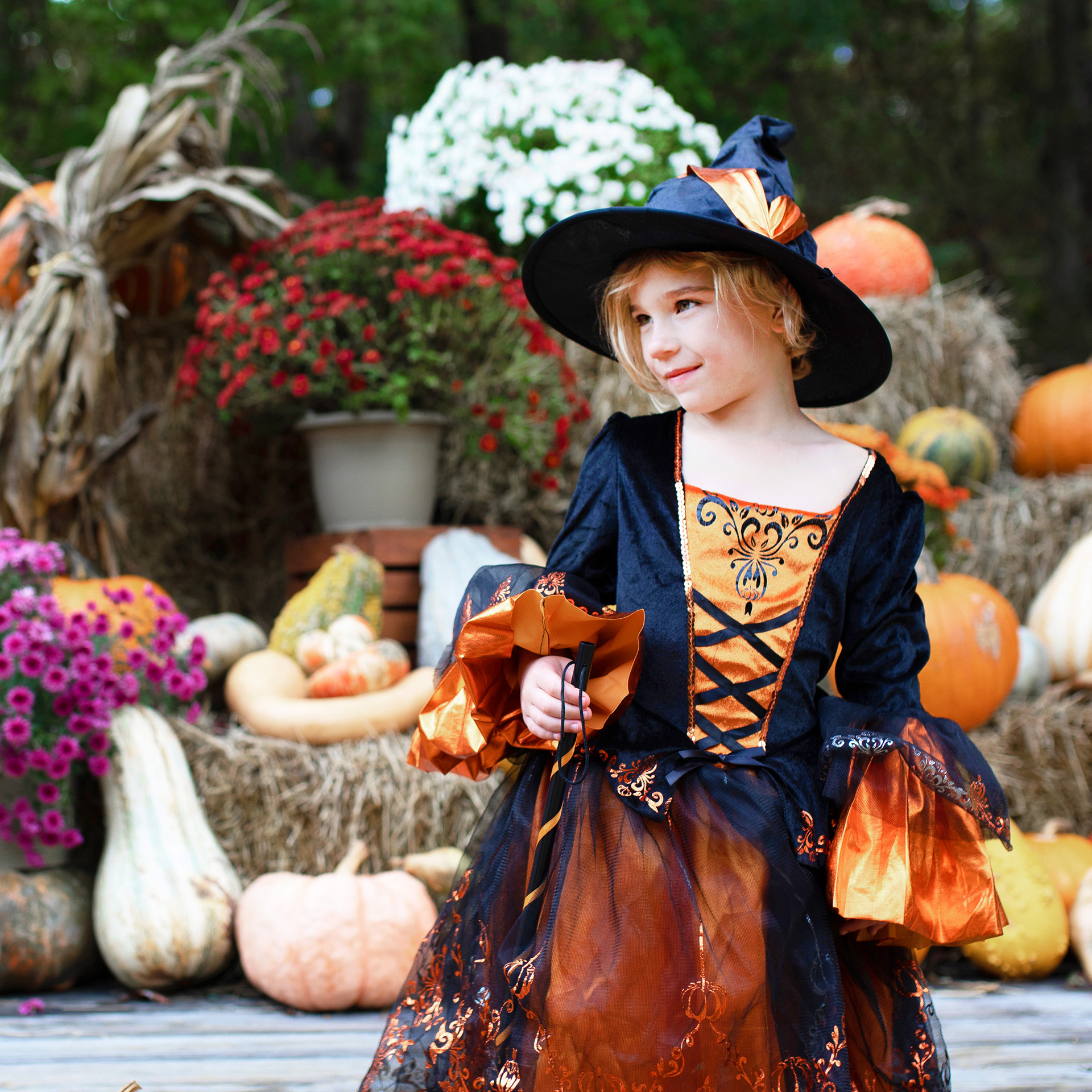 A young girl wears a witch costume near bales of hay.