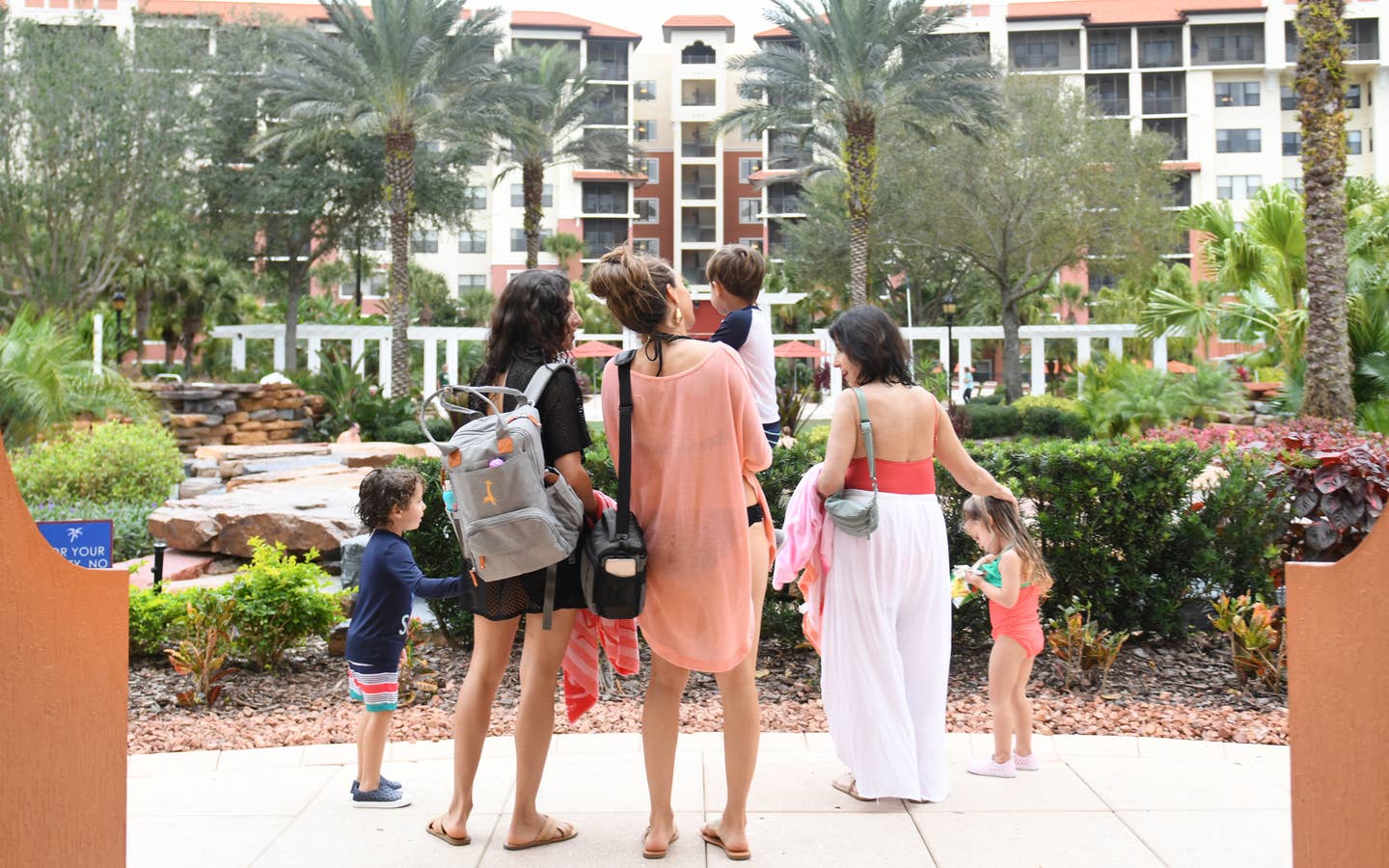 Family standing outside of a large resort building with large palm trees and tropical plants