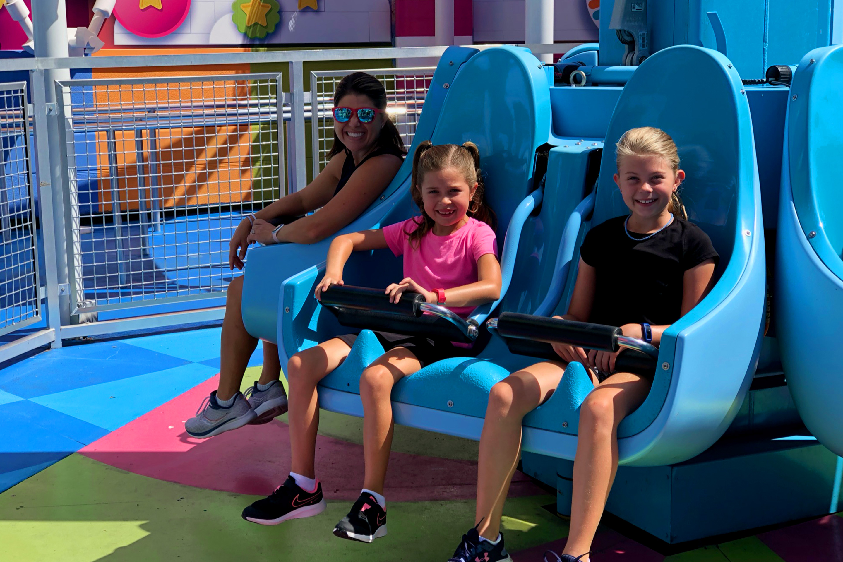 A woman (left) and two girls (right) are seated on a vertical ride vehicle.