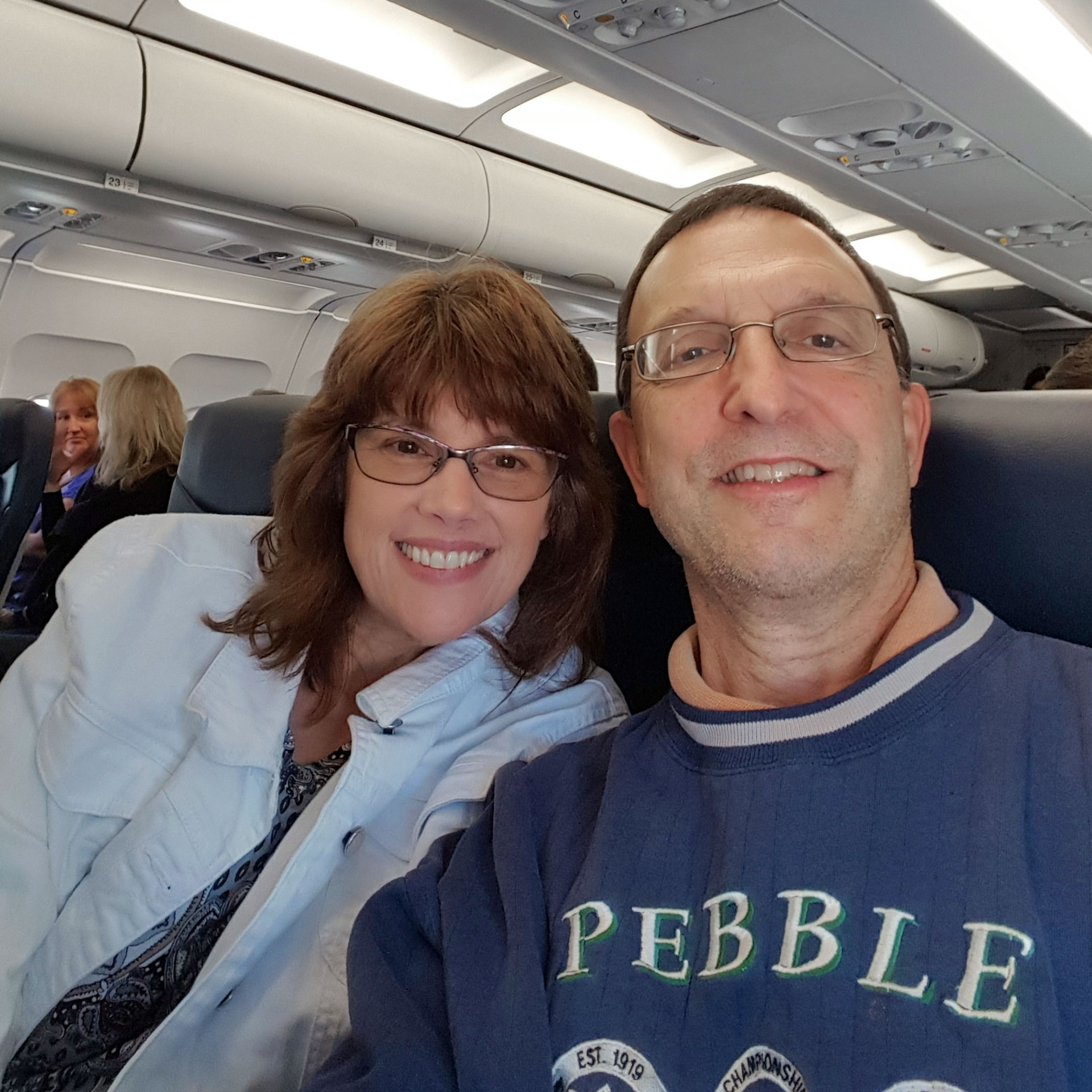 A woman in a white coat and a man in a navy pullover are seated on an airplane. Image taken before COVID-19.