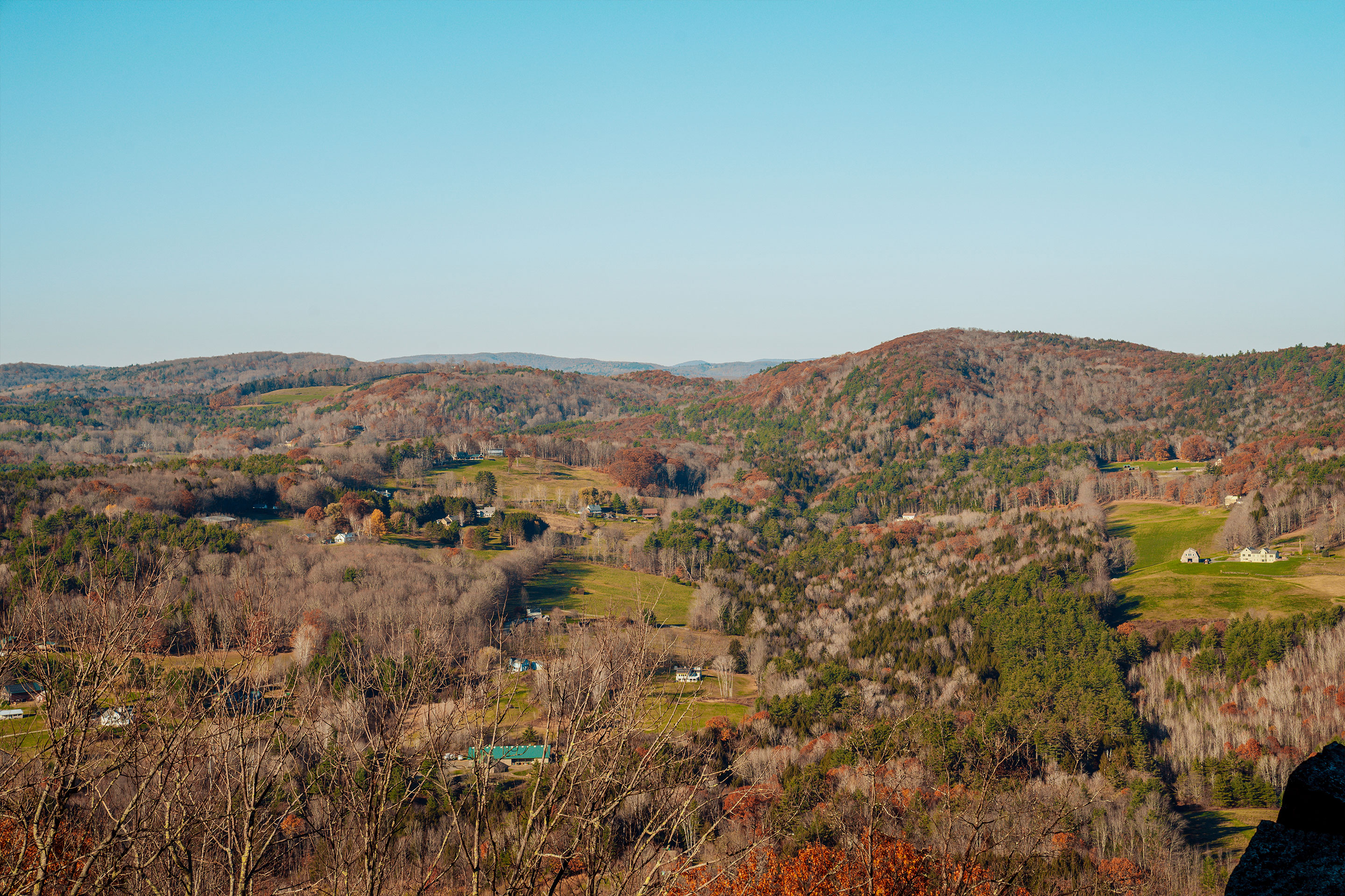 A mountain range covered in trees showing early fall foliage underneath a blue sky.