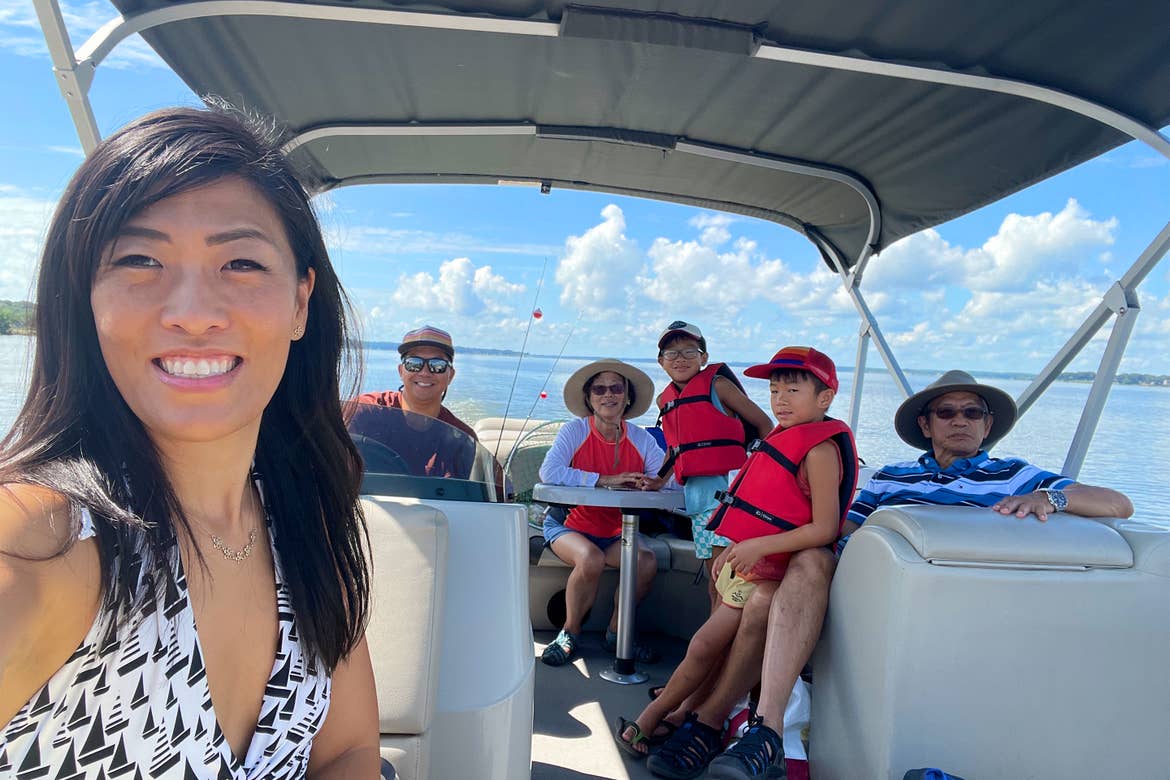 An Asian woman wearing a white swimsuit on a boat with her multigenerational family on a lake.