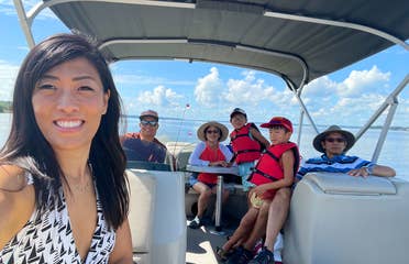 An Asian woman wearing a white swimsuit on a boat with her multigenerational family on a lake.
