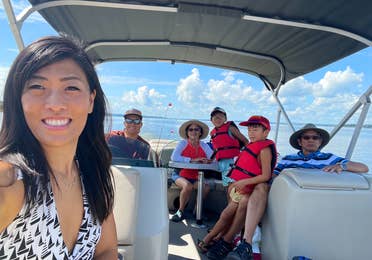 An Asian woman wearing a white swimsuit on a boat with her multigenerational family on a lake.