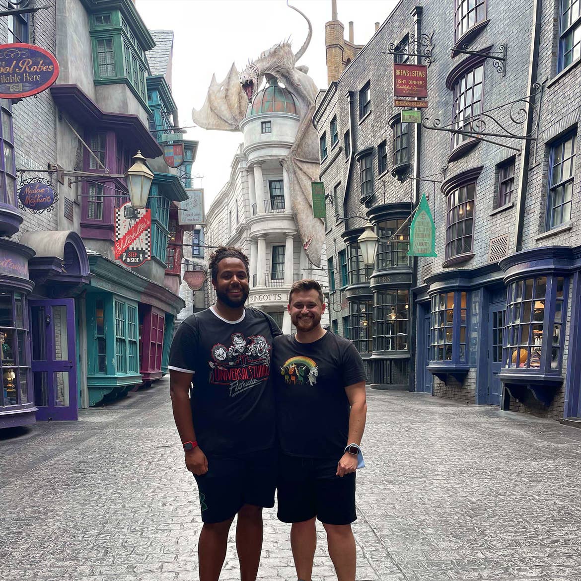 Two men wearing black t-shirts and shorts stand in front of Diagon Alley at Universal Orlando.