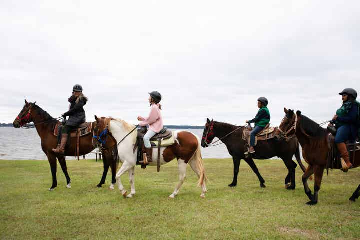 Four people horseback riding near a body of water
