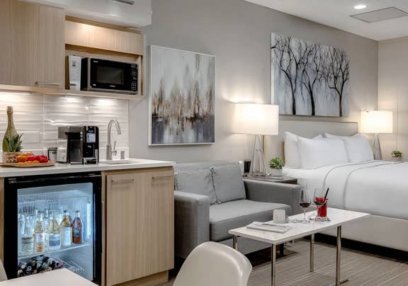 Hotel room featuring dark cabinetry kitchenette, sleek countertop, cozy living area, and city views.