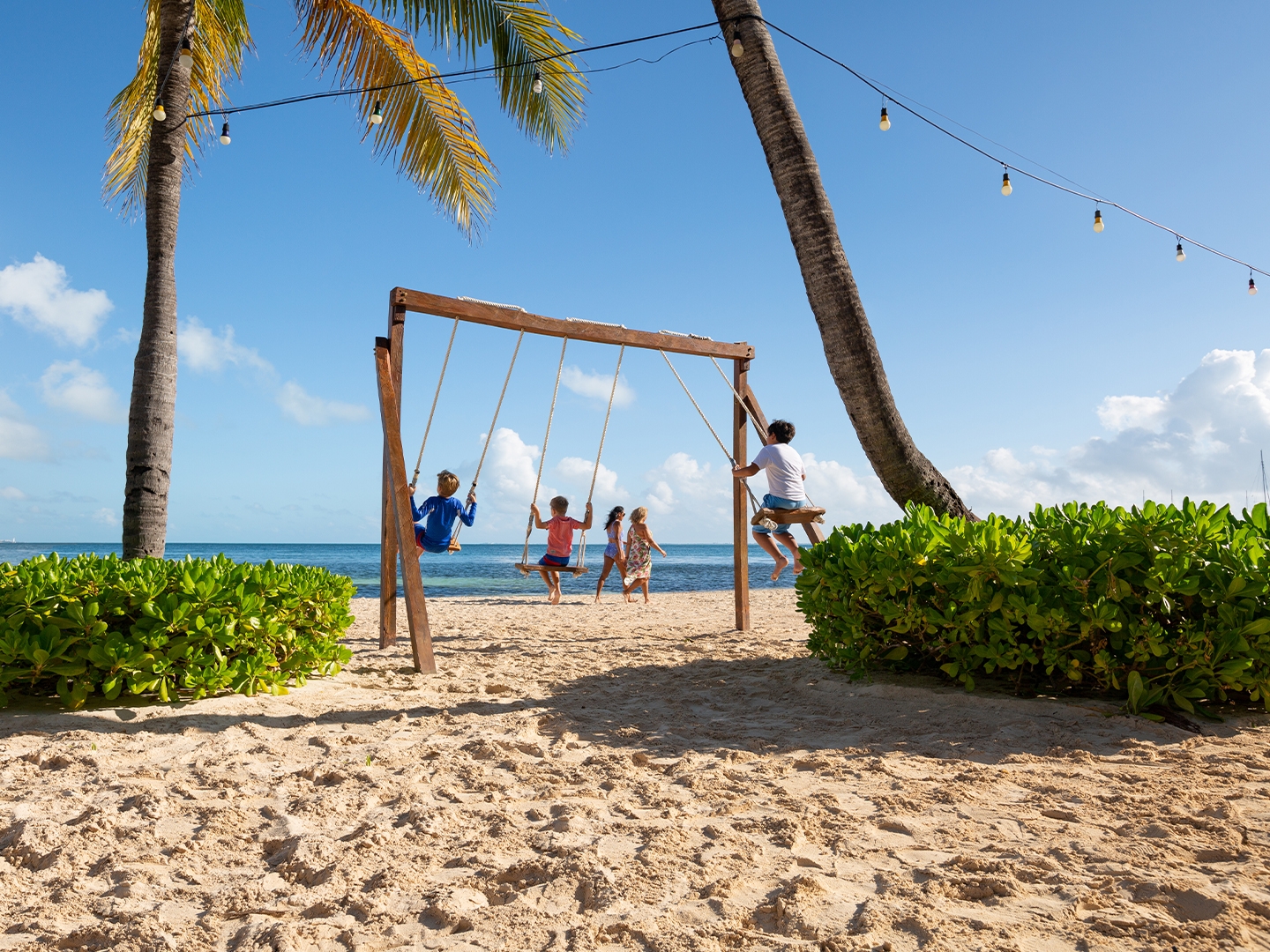 Three kids the beach swinging on a swingset at Royal Cancun Resort in Mexico.