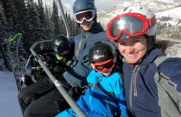 Author, Jessica Averett, and her family sit on the ski lift in winter apparel and ski gear.
