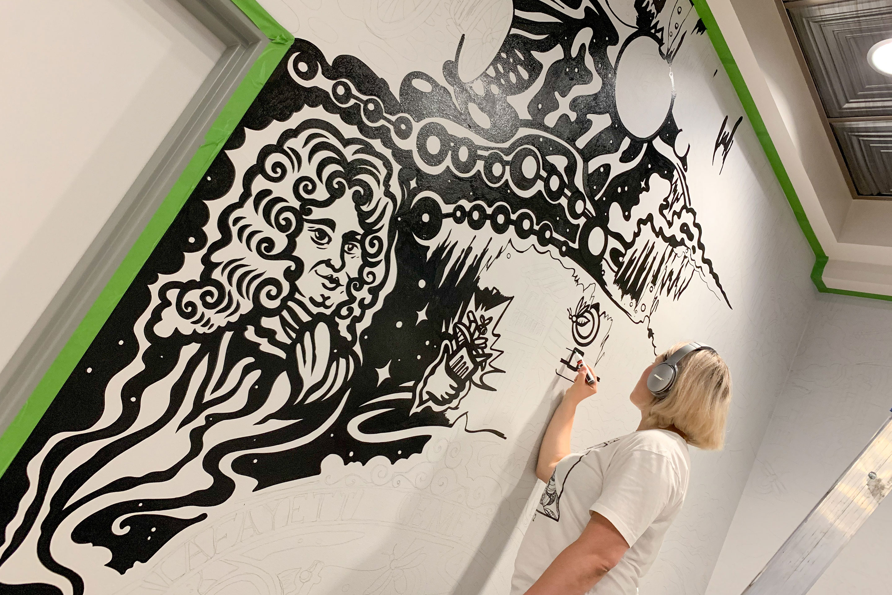 Muralist, Mila Sketch, wears headphones as she paints over her outlined mural art featured in the lobby of our resort in New Orleans, Louisiana.