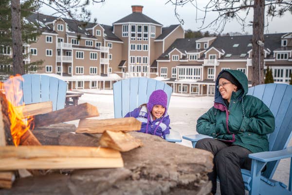 A woman and a young girl sitting by the fire pit in the winter in front of Mount Ascutney Resort