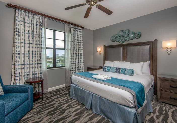 Bedroom with king bed, large window, seating area, and ceiling fan in a three-bedroom villa at Sunset Cove Resort in Marco Island, Florida