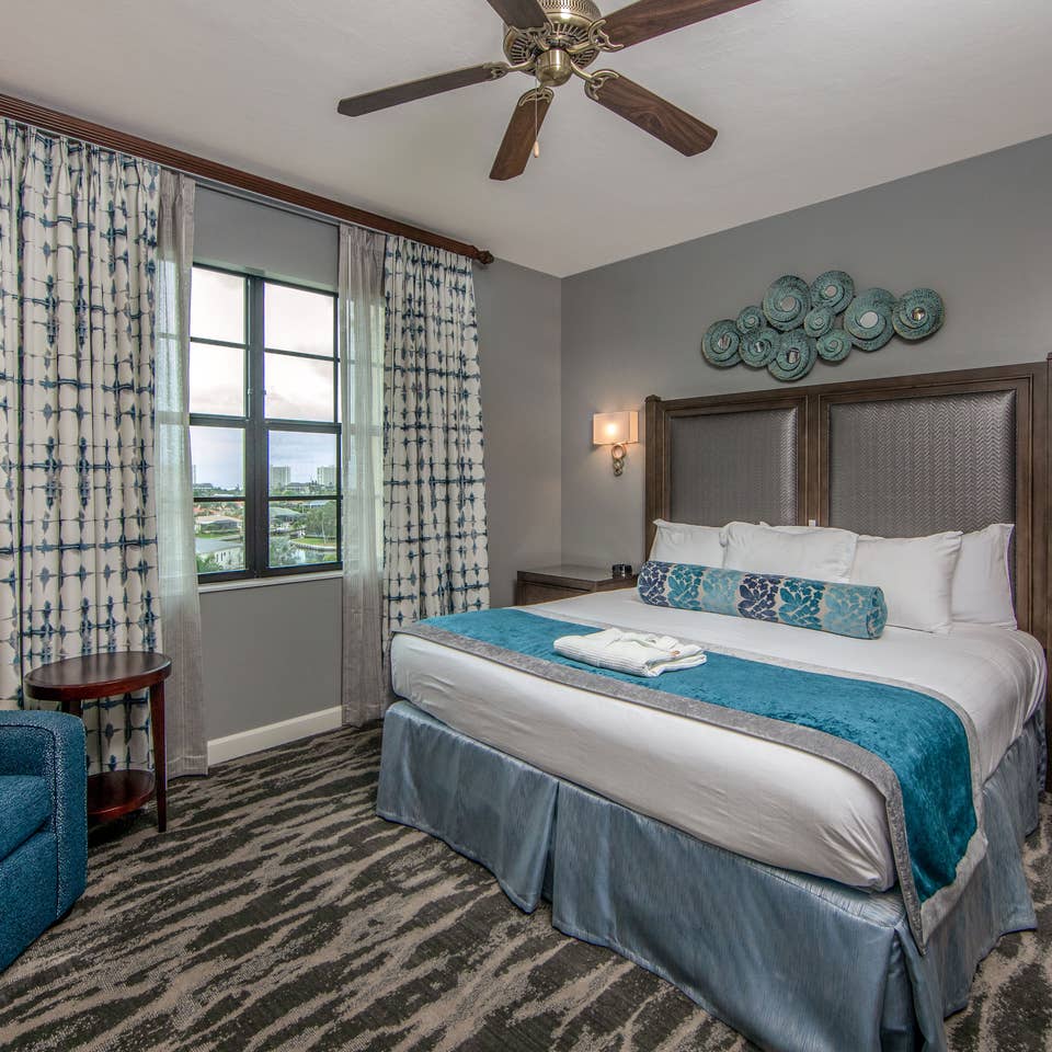 Bedroom with king bed, large window, seating area, and ceiling fan in a three-bedroom villa at Sunset Cove Resort in Marco Island, Florida