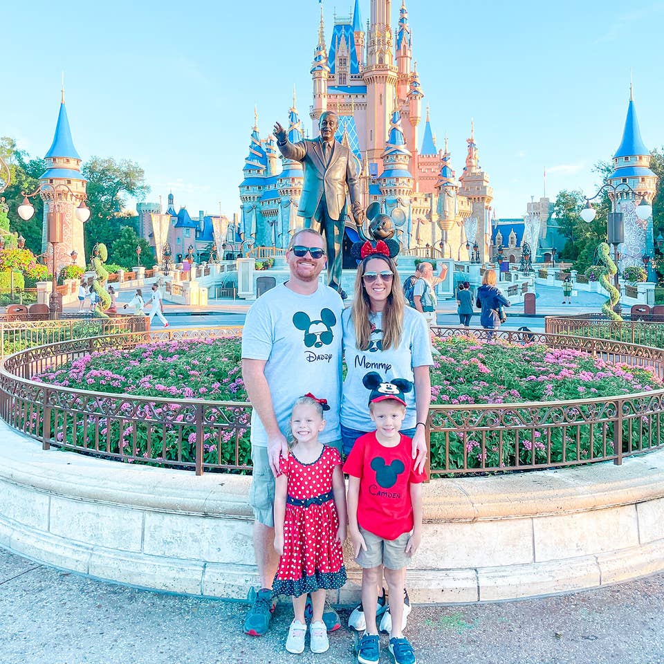A man, woman, boy and girl stand wearing Disney apparel in front of Cinderella's Castle in Walt Disney World.