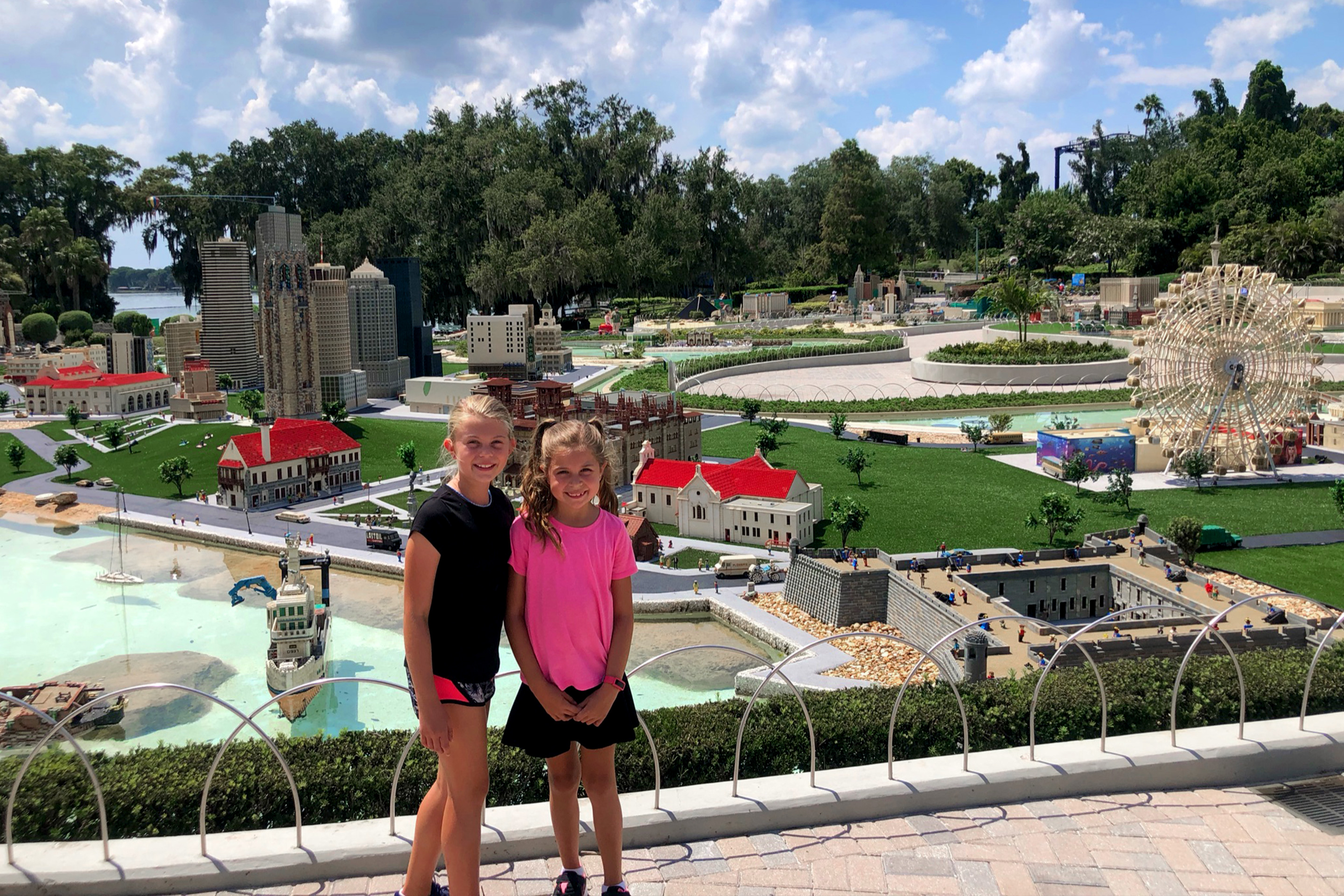 Two young girls stand in front of a scaled city made entirely of LEGOS.