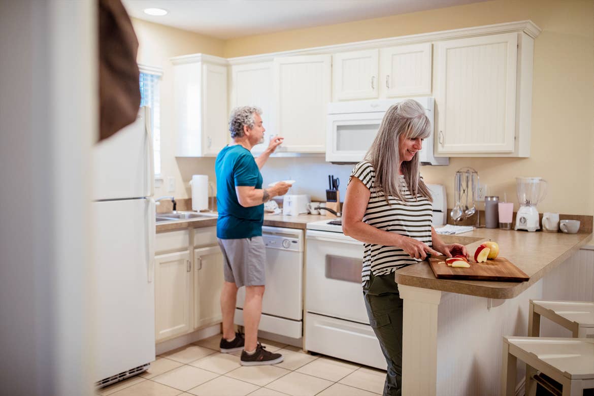 An older couple stand in a kitchen prepping food.