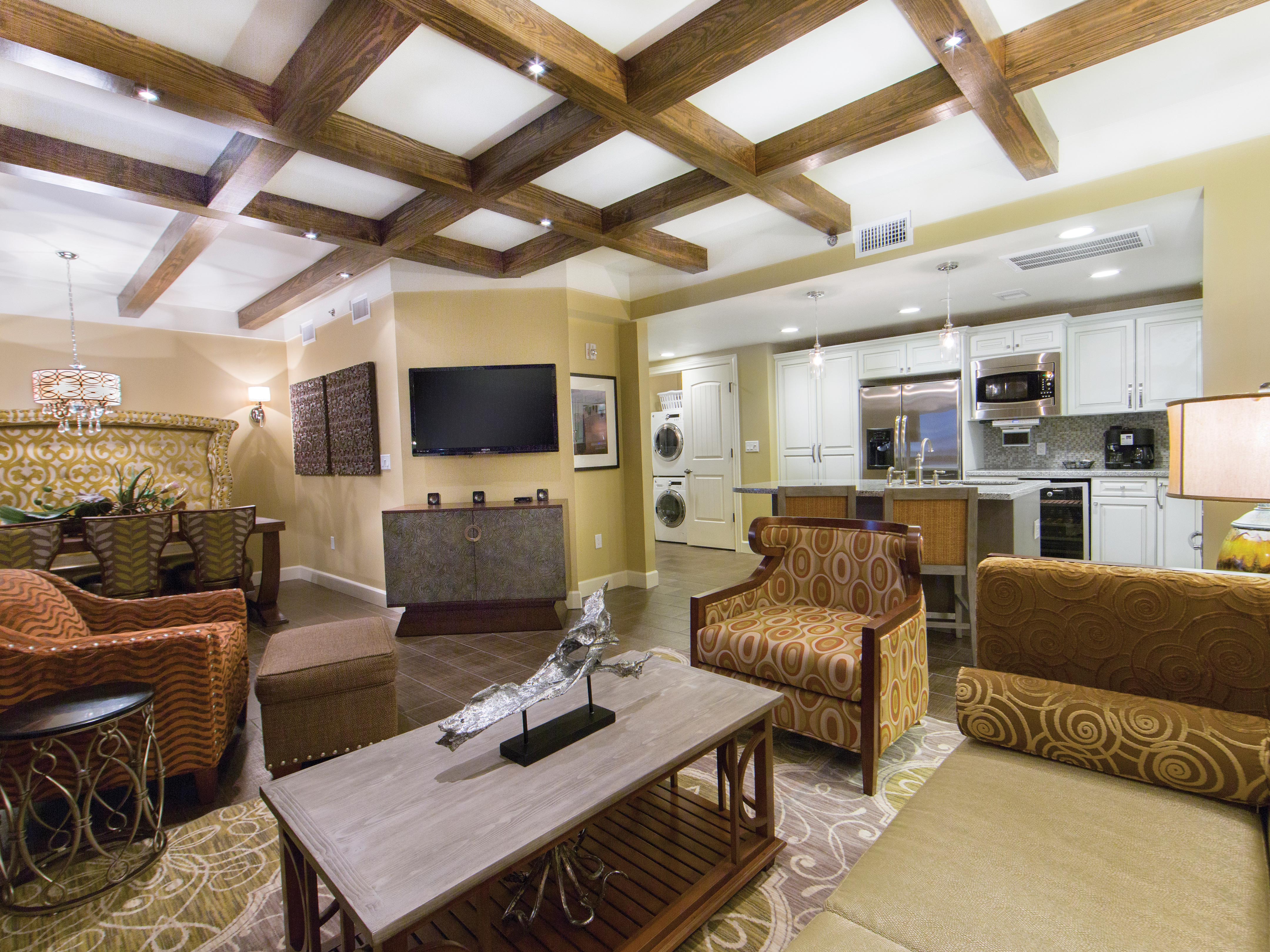 Living room with flat screen TV, couch, two accent chairs, and a view of the kitchen in a Signature two-bedroom villa at Galveston Beach Resort