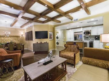 Living room with flat screen TV, couch, two accent chairs, and a view of the kitchen in a Signature two-bedroom villa at Galveston Beach Resort