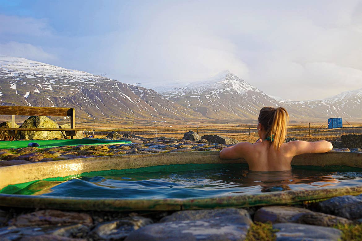 Featured Contributor, Ashlyn George, sits in a hot spring looking at the mountains of Iceland.
