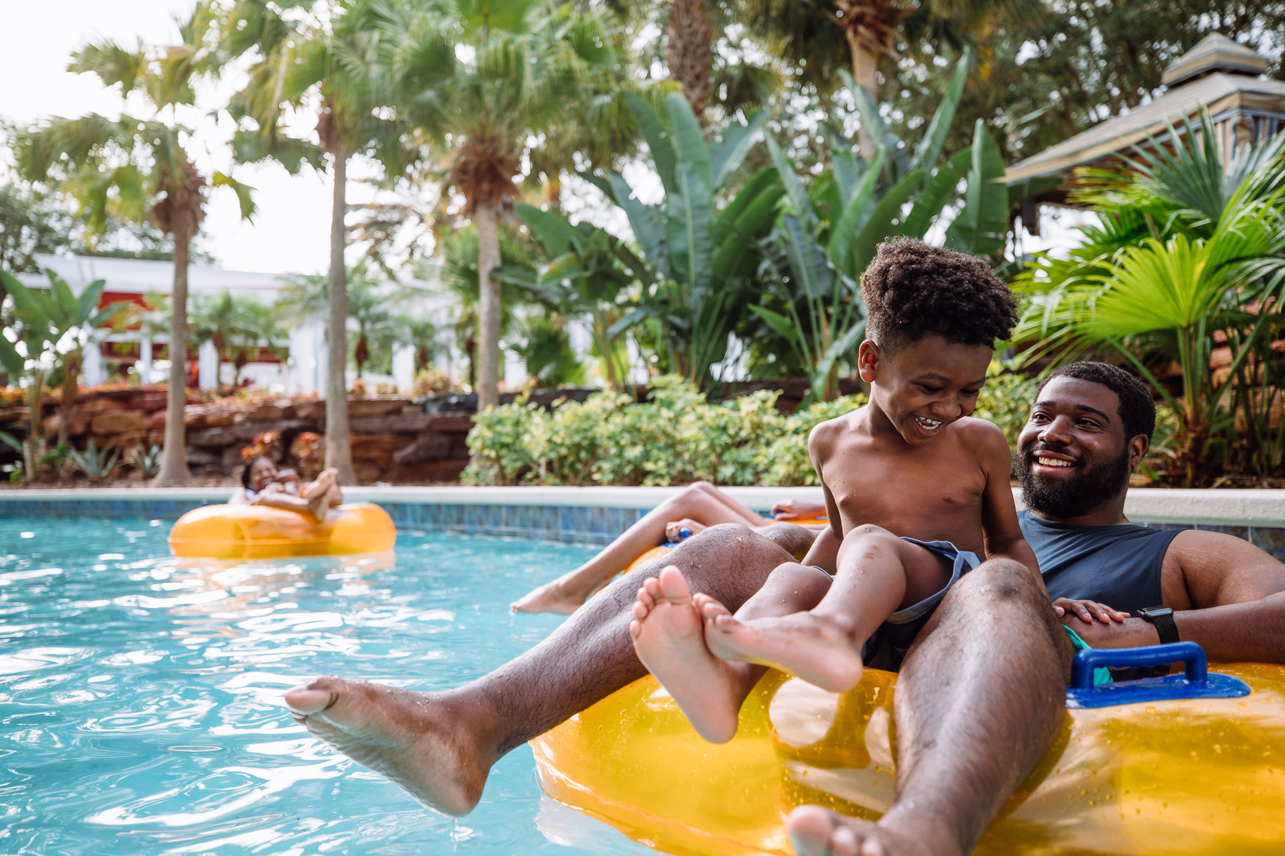 A man and young boy share an inner tube down a lazy river.