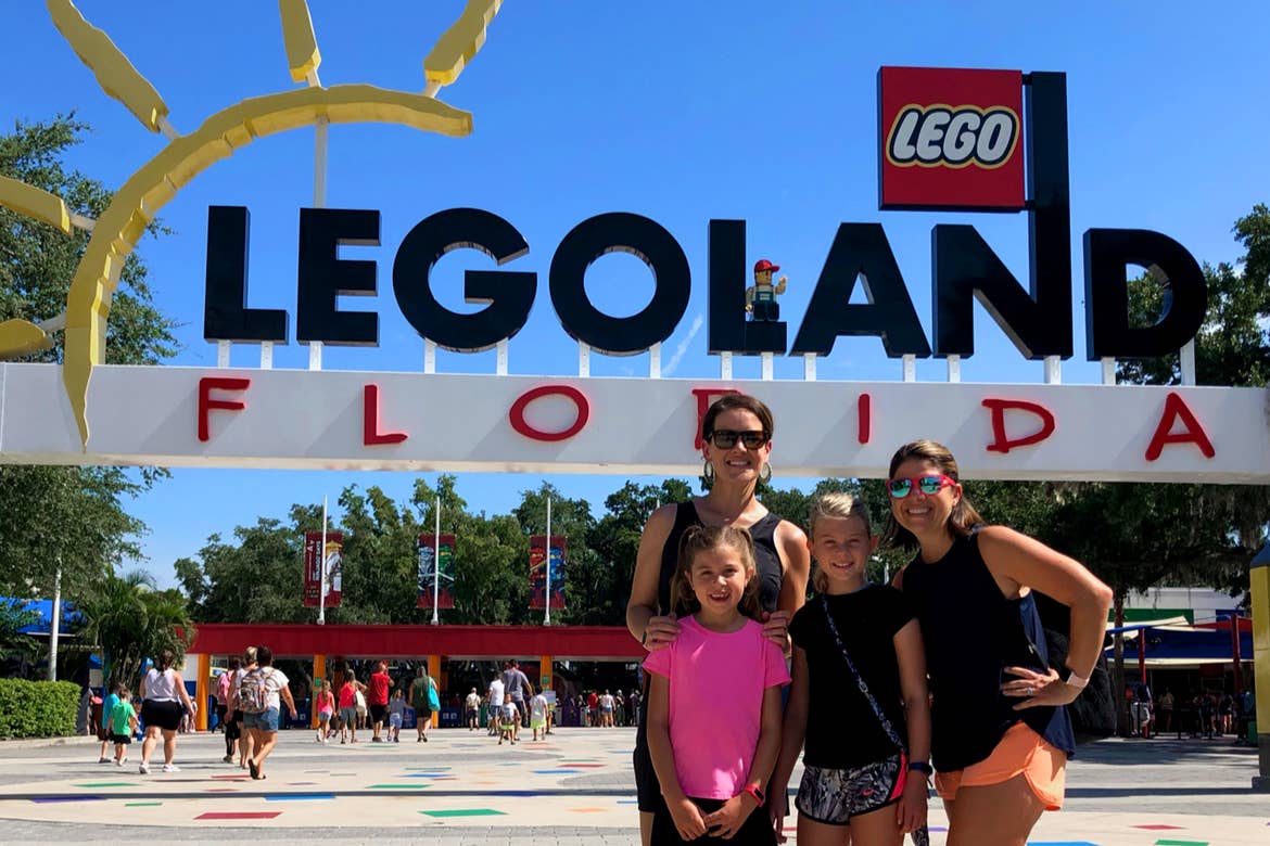 Two women (back) and two young girls (front) stand in front of a LEGOLAND sign in Orlando.