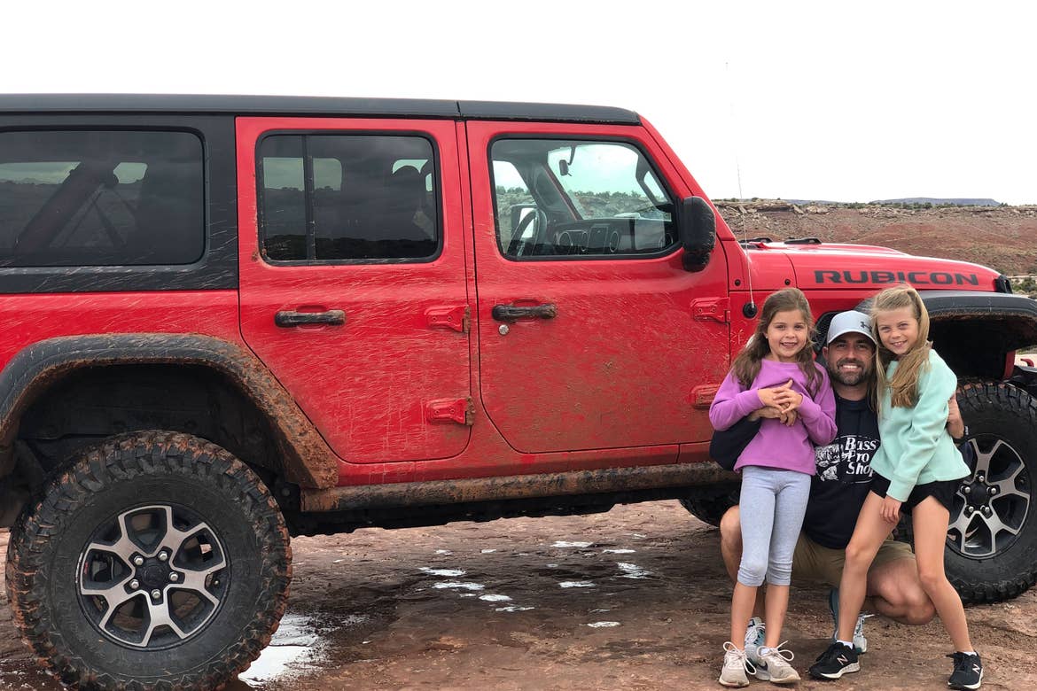 Josh (middle) and daughters (left and right) pose in front of their red Jeep Rubicon for some off-roading adventures.