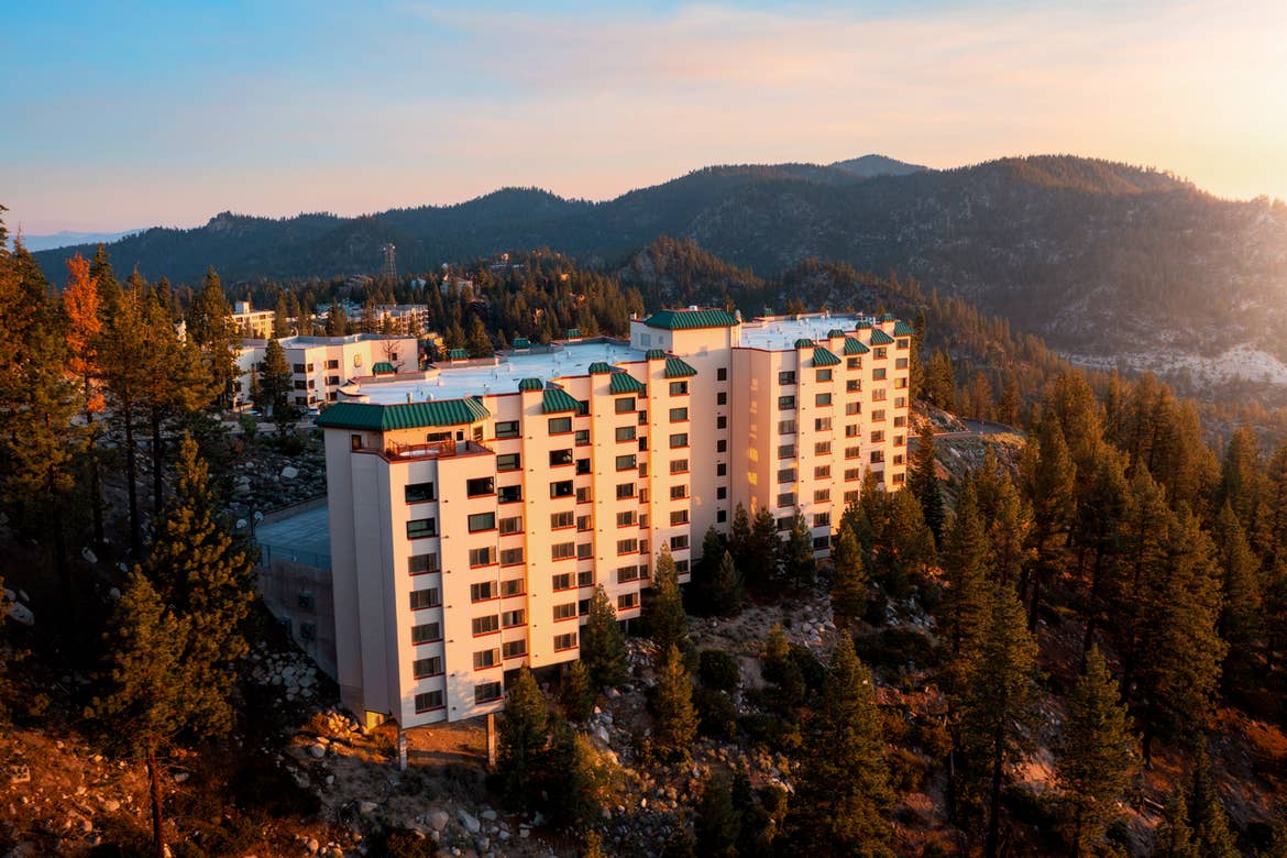 A drone view of our Tahoe Ridge Resort exterior located in Lake Tahoe, Nevada surrounded by pine trees of various heights and the mountain ridge as the sun sets.