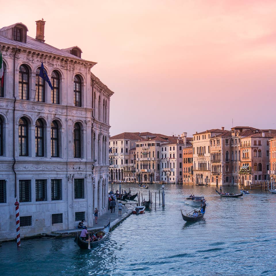 The rivers of Venice with gondolas and structures under sunset pink skies.