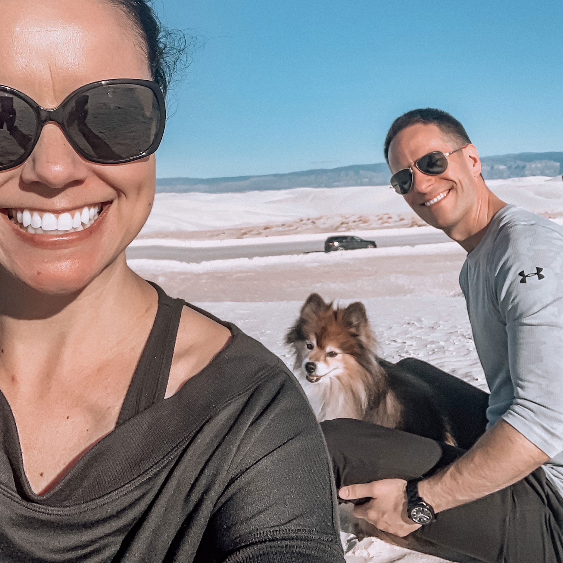 Authors, Lauren Layne and Anthony LeDonne, sit in front of their vehicle with Bailey the Pomeranian at the White Sands National Monument.