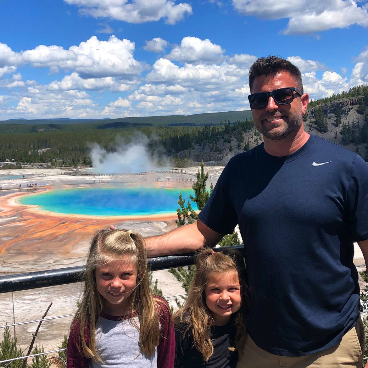 Author, Chris Johnstons' husband, Josh (far-left), stands in front of the Grand Prismatic Springs Springs at Yellowstone National Park with their daughters, Kyndall (front-left), and Kyler (front-right).