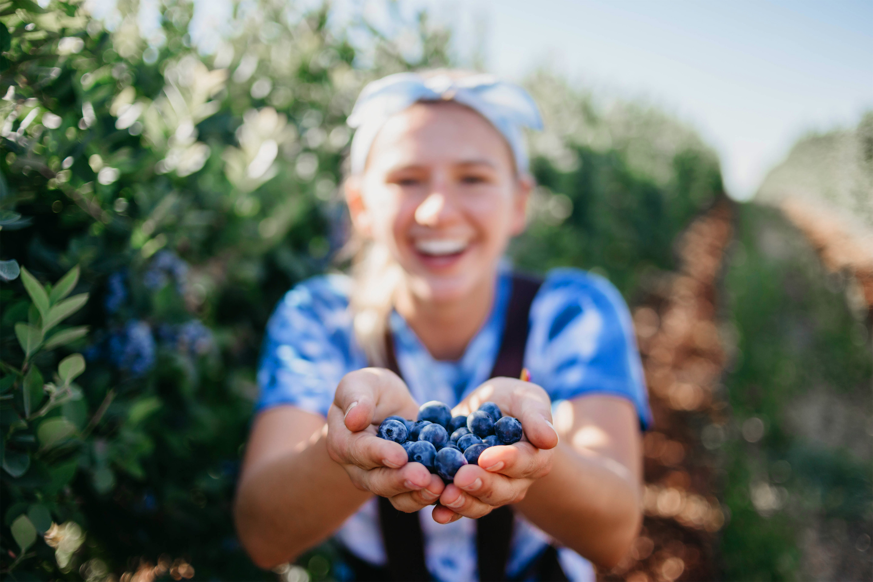 A woman holds a bunch of blueberries in hand outdoors.