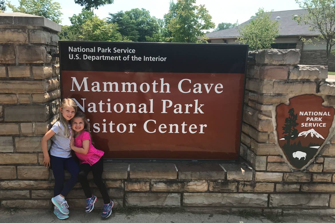Author, Chris Johnstons' daughters, Kyndall (left), and Kyler (right) pose with a sign that reads, 'National Park Service, U.S. Department of the Interior, Mammoth Cave National Park Visitor Center.'