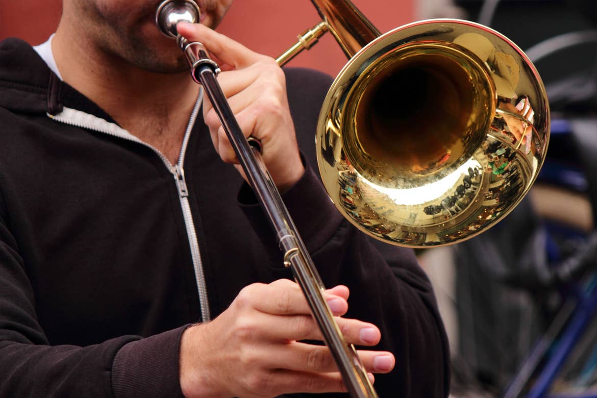 Jazz performer wearing a black zip-up hoodie plays a gold trombone on the streets of New Orleans.