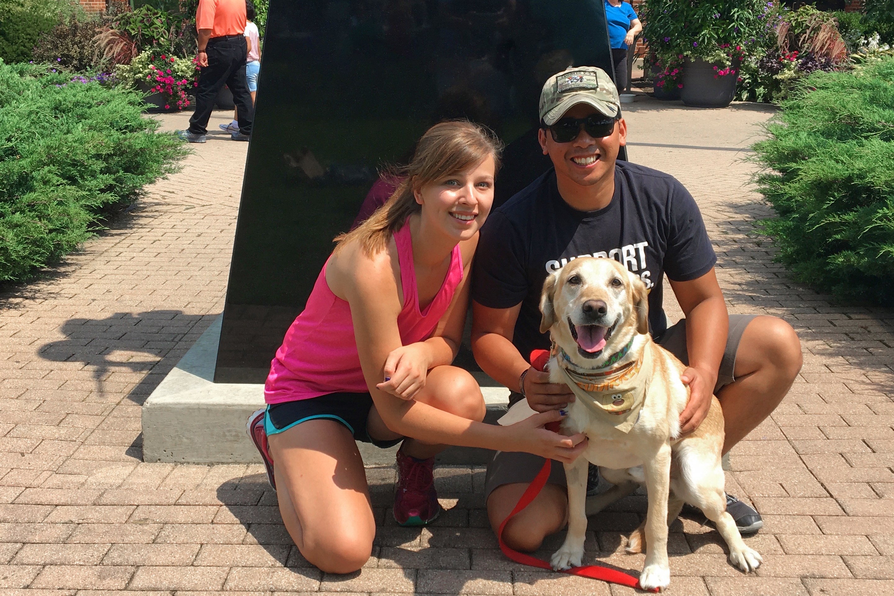 A woman (left) a man (right) and a dog (front) stand in front of a statue.