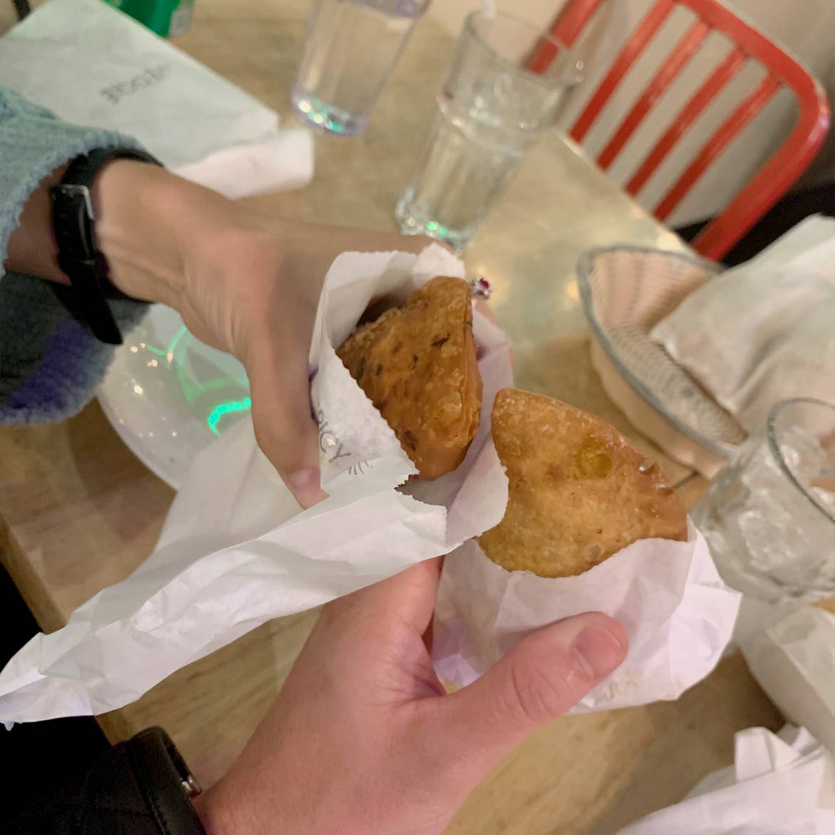 The hands of a Caucasian male and female hold a pair of empanadas over a table.